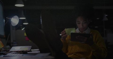 Woman Relaxing with Tablet and Cup in Nighttime Office