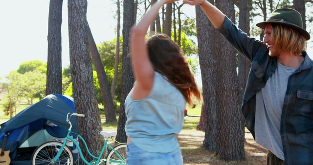 Young couple enjoying a spontaneous dance in a forest near their campsite. Perfect for promoting camping trips, outdoor adventures, vacations, and lifestyle blogs centered around nature and outdoor activities.