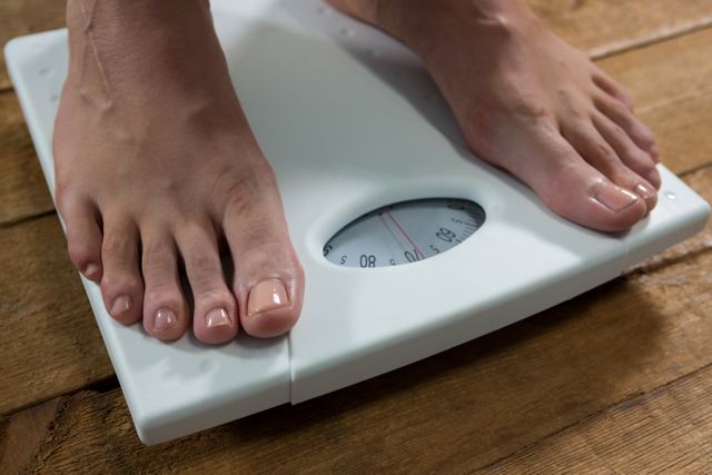 This image shows a woman's feet on a weighing scale, indicating a focus on health and fitness. It can be used in articles or advertisements related to weight management, fitness programs, health tips, and lifestyle changes.