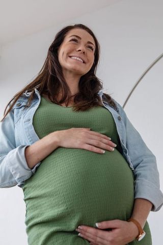 Pregnant Woman Smiling Holding Belly in Cozy Home Interior