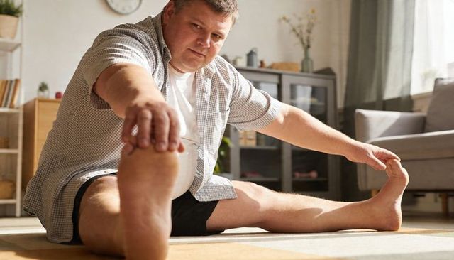 Middle-aged man stretching on living room rug improving mobility and flexibility