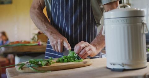 Senior Man Cutting Vegetables in Home Kitchen with Compost Bin
