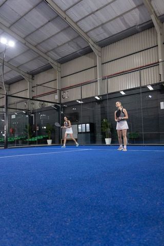 Female partners practicing padel doubles on vibrant blue indoor court in matching outfits