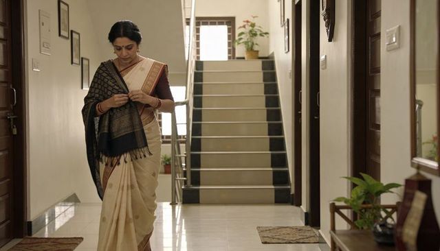 Middle-aged indian woman walking in home hallway adjusting shawl over traditional sari