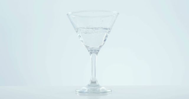 A clear liquid, water or a transparent beverage, is partially filling a martini glass against a white background, with copy space. The simplicity of the image suggests a minimalist approach, ideal for backgrounds or beverage-related themes.