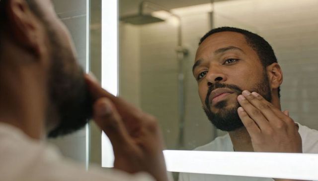 Man inspecting beard in led-lit bathroom mirror during grooming routine
