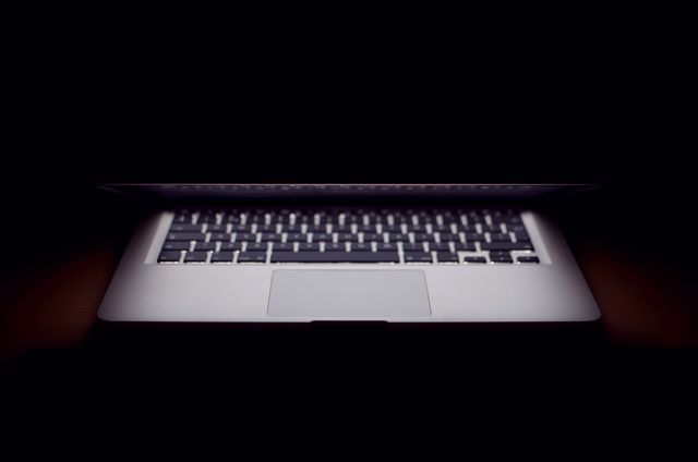 Illuminated partially-open laptop with dark background emphasizing modern technology and gadgets. Perfect for technology blogs, electronics advertisements, digital marketing material, and articles about modern workspaces and internet culture.
