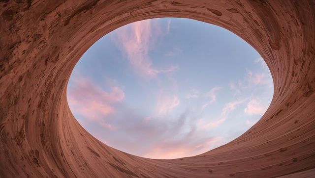 Curved timber oculus framing pastel sunrise sky through oval skylight with wood grain