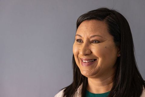Warm mature woman smiling and posing in studio headshot with gray backdrop and green top