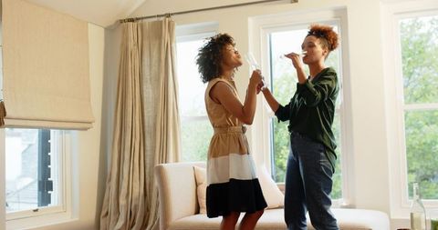 African American women toasting champagne flutes in sunlit modern living room celebration
