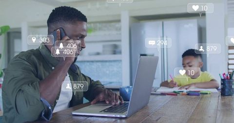 Busy father juggling remote work and child learning at kitchen table with digital alerts