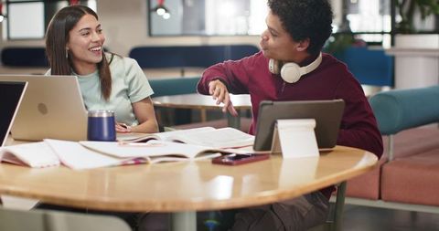 College students collaborating over laptops and notes at campus lounge roundtable