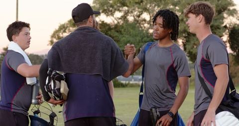 Youth football team greeting coach during sunset practice on grassy field
