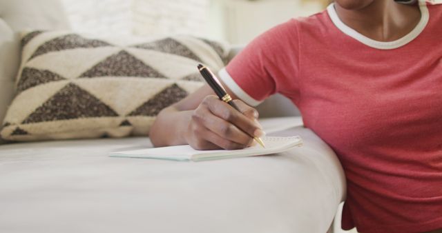 Person writing in notebook at home wearing red casual shirt - Download Free Stock Images Pikwizard.com