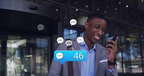 Young black businessman smiling while checking mobile messages at modern glass office entrance