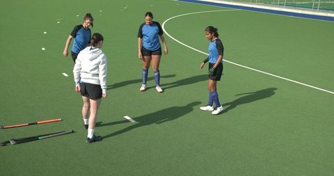 Female field hockey players strategizing on green turf