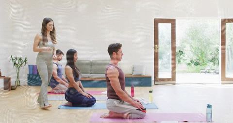 Yoga instructor guiding small class kneeling meditation in sunlit studio with garden view