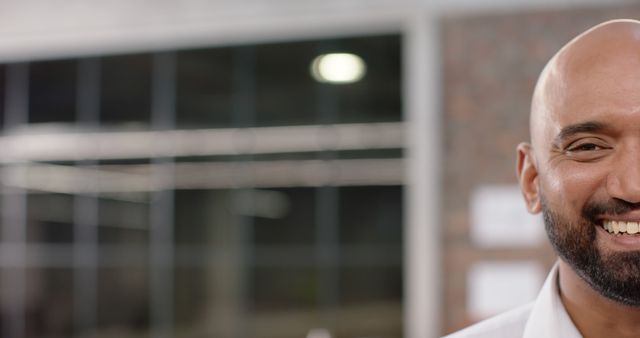 This close-up of a smiling man in a professional office setting can be used in marketing materials, corporate websites, advertisements, or presentations to convey a friendly and approachable workplace environment. It is great for depicting positive workplace culture, employee satisfaction, or corporate communications.