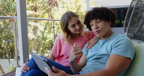 Young Couple Relaxing on Sunny Balcony Watching Tablet