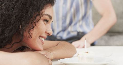 Smiling Woman Watching Candlelit Cupcake at Birthday Celebration