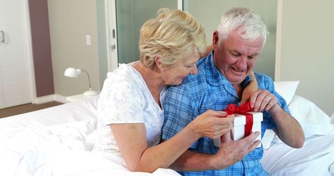 Joyful senior couple present exchange in bedroom