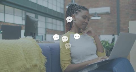 Young professional woman working remotely on laptop in modern coworking loft, contemplating