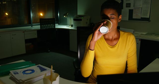Biracial female casual businesswoman drinking coffee using computer in office at night, copy space - Download Free Stock Photos Pikwizard.com