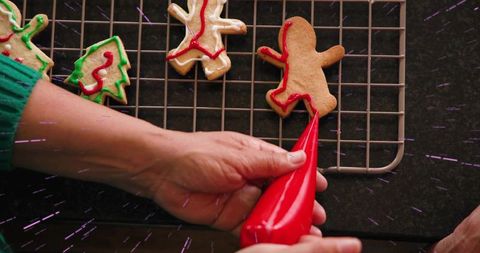 Hands piping red icing on gingerbread cookies for festive holiday baking