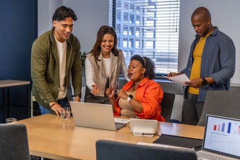 Diverse team celebrating successful data presentation around laptop in modern boardroom