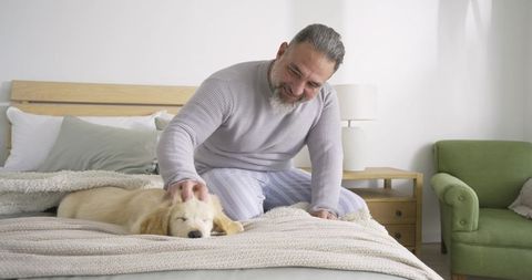 Senior Man Bonding with Golden Retriever Puppy in Cozy Bedroom