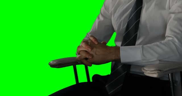 Businessman in formal attire sitting on office chair with green screen background. Ideal for corporate, business or professional presentations, video interviews, and promotional marketing materials.