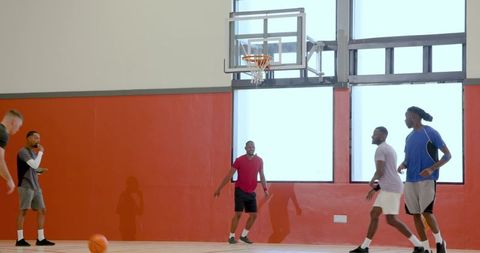 Young men playing indoor basketball team practicing drills near hoop in bright gym