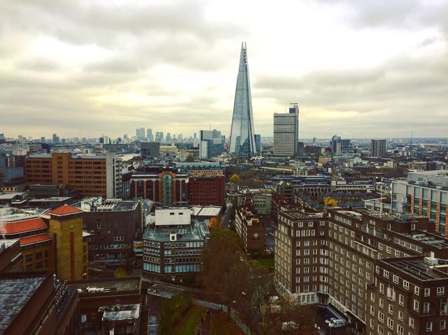 Panoramic view of London with prominent view of The Shard amidst numerous buildings on an overcast day. Perfect for projects needing images of urban exploration, architecture studies, city life, travel brochures, and backgrounds indicating metropolitan vibes.