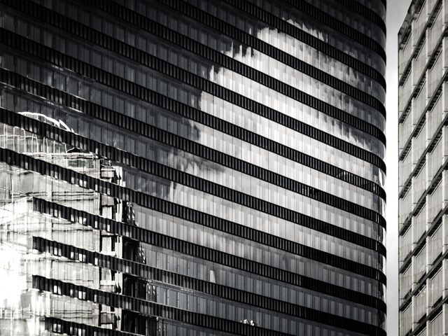 This image captures the exterior of modern glass skyscrapers reflecting clouds in a black and white palette. Ideal for use in corporate presentations, architectural studies, urban development projects, and contemporary design showcases. The monochrome tone adds a timeless and sophisticated touch, conveying themes of modernity and corporate elegance.