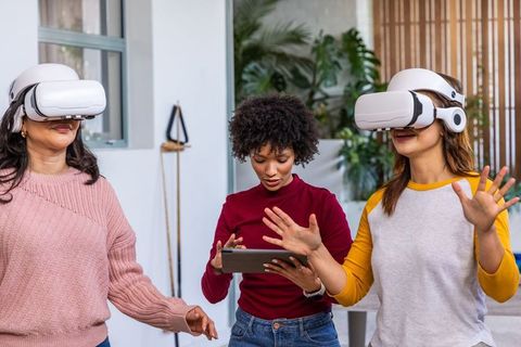Diverse women testing virtual reality headsets in coworking office, tablet-guided demo