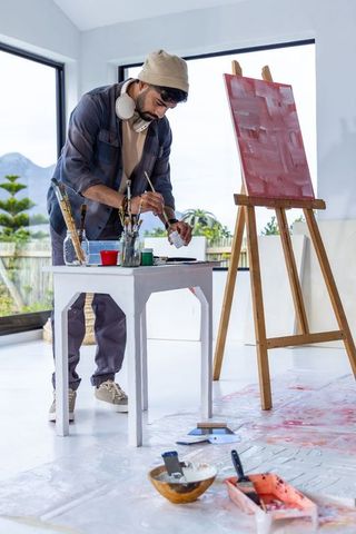 Asian male artist painting abstract red canvas in bright sunlit modern studio