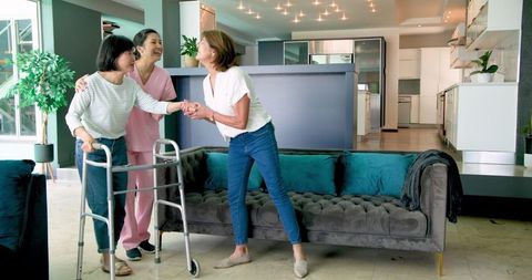 Senior Woman with Walker Smiling with Nurse and Friend in Modern Apartment