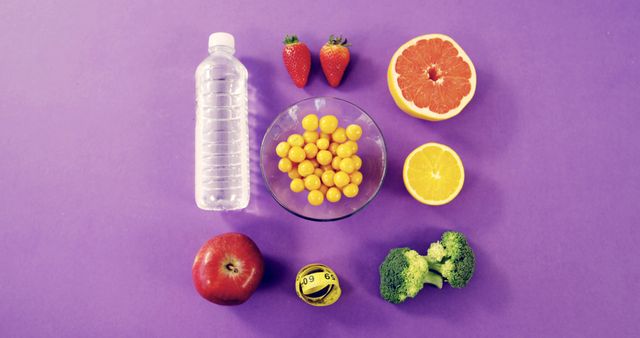 This colorful arrangement featuring a variety of fresh fruits and vegetables, with a bottle of water, can be used in promoting healthy eating habits and diet plans. The vibrant purple background creates visual appeal, making it perfect for websites, blogs, and marketing materials focused on nutrition, wellness, and organic food products.