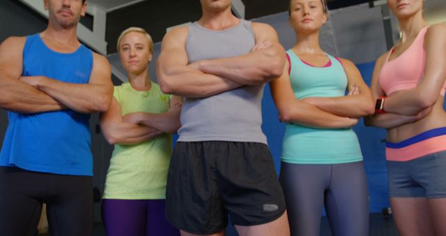 Group of dedicated fitness enthusiasts posing with folded arms in modern gym. Ideal for advertising fitness programs, promoting gym memberships, or showcasing teamwork in a health and wellness context.