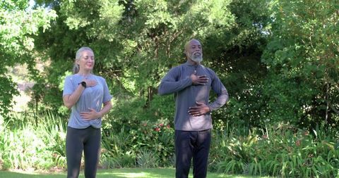 Diverse couple practicing mindful breathing in sunlit garden wearing sportswear