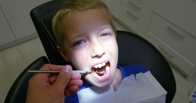 Young boy in dental clinic receiving examination from a dentist. Dentist using oral instrument to check child's teeth and oral health. Can be used for medical and healthcare topics, brochures for pediatric dentistry, or health and hygiene education.