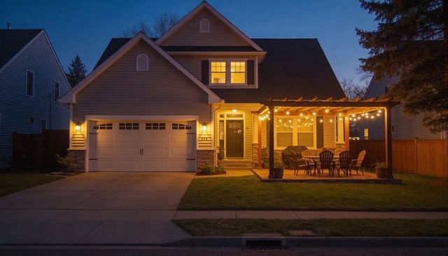 Glowing suburban two-story home with warm interior lights and string-lit pergola patio