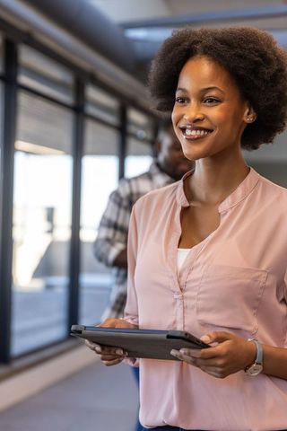 Smiling businesswoman holding tablet in modern office corridor