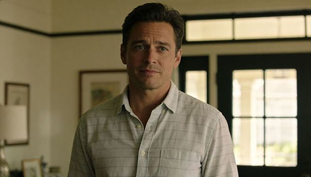 Man in casual checked shirt standing in bright home entryway, thoughtful expression