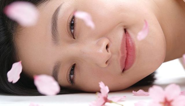 Serene asian woman reclining amid falling pink cherry blossom petals closeup portrait