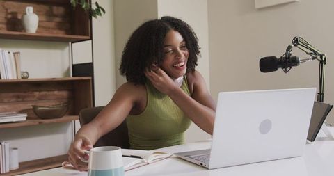 African american creator podcasting from cozy home desk with laptop microphone and mug
