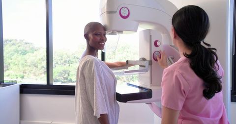 African American woman receiving mammogram from Asian technician in bright clinic room