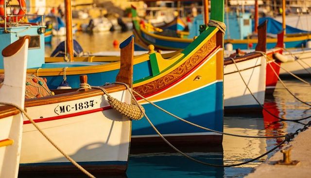Resting colorful maltese luzzu boats lining harbor quay during golden hour reflections