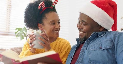 Smiling black couple enjoying cozy holiday morning on couch with santa hat and hot drink