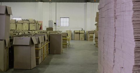 Industrial warehouse stacking tall flat cardboard sheets in aisle with pallets and boxes